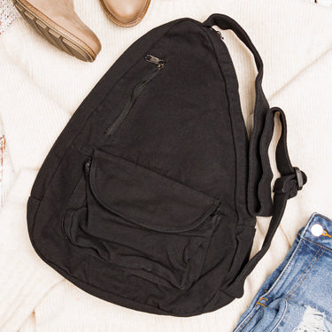 Black sling bag on a light wooden surface with a shoe and jeans in the background