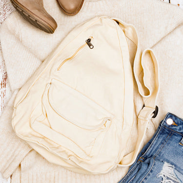 Cream crossbody bag with zippers, brown boots, and blue jeans on a textured surface