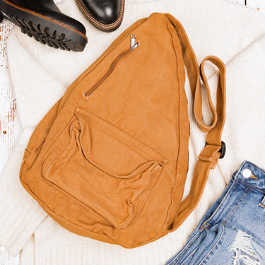 Brown sling bag on a light wooden surface with a boot and jeans.