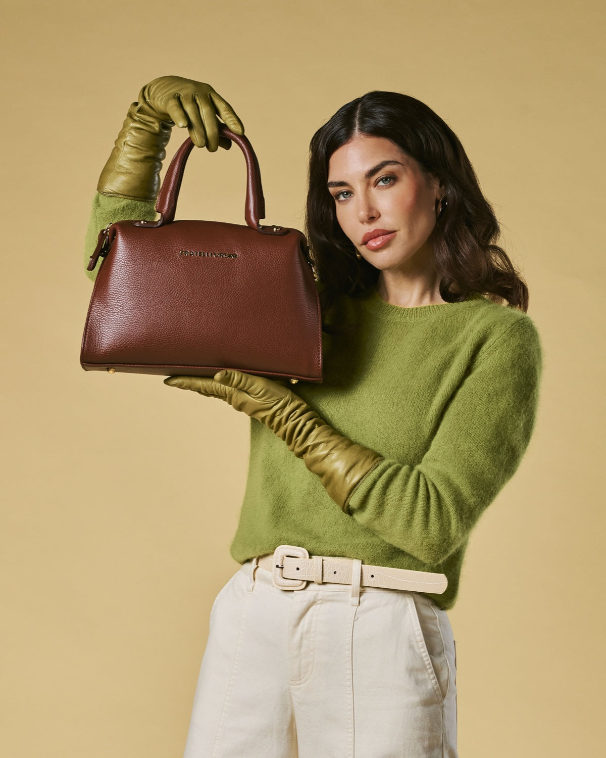 Woman holding a brown handbag against a beige background