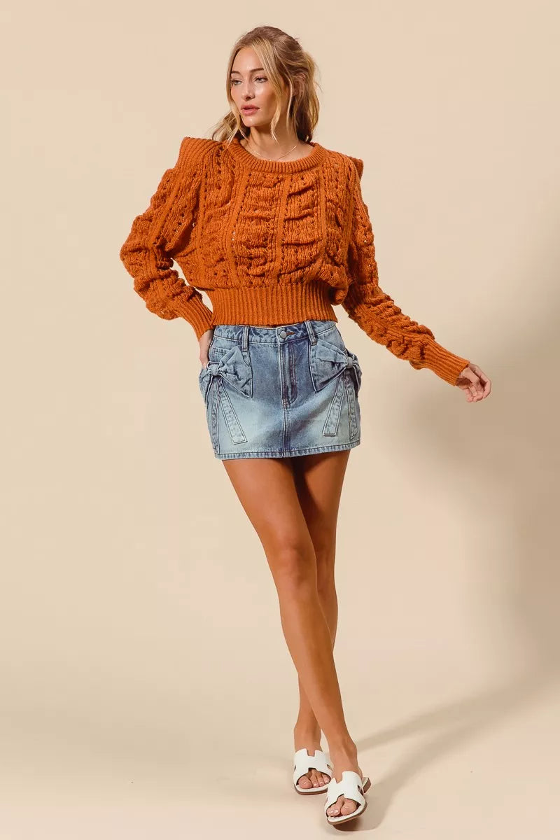 Model wearing an orange cable knit sweater and denim skirt with statement bows