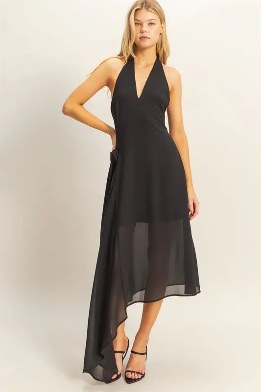Black halter midi dress featuring an asymmetrical handkerchief hem and fabric rosette detail at the hip.