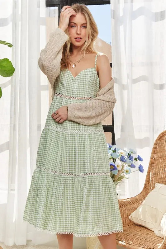 Woman styling a sage gingham midi dress with a neutral knit cardigan for an elevated daytime look.