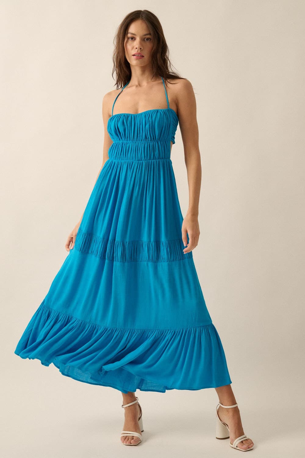 Studio shot of model in blue maxi dress with halter neckline, ruched bodice, and flowing ankle-length hem.