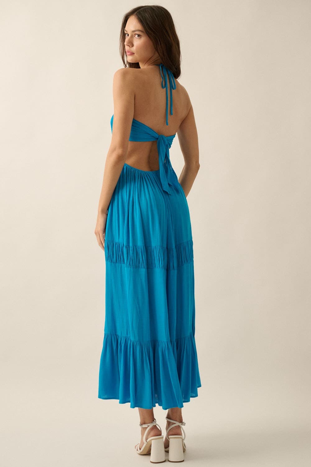 Back view of the blue halter neck dress highlighting the self-tie straps and open-back design in studio lighting.