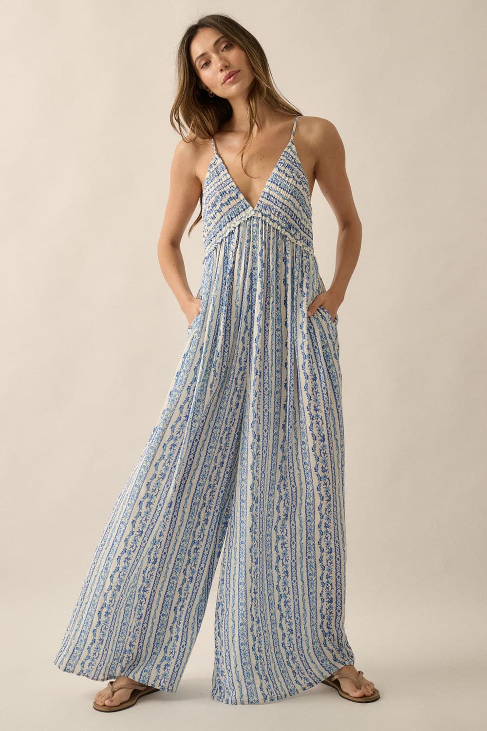 Studio front view of jumpsuit showcasing deep V-neckline, smocked bodice, and wide-leg flow