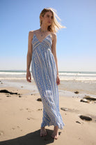 Model wearing blue and white floral wide-leg jumpsuit walking barefoot on the beach under blue skies-AVAH