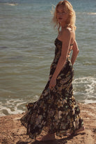 Side view of model in strapless floral maxi dress with open strappy back walking by the ocean