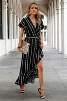 Model in black striped maxi dress with V-neckline and tie waist, holding neutral boho clutch.