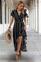 Black and white wrap dress with flutter sleeves and a leg-baring front slit, styled with heels and a textured clutch.