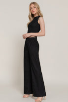 Model  wearing a black matching set with wide-leg pants and sleeveless top on a plain background