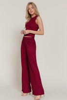 Side profile of model  wearing a red matching set with wide-leg pants and sleeveless top on a plain background