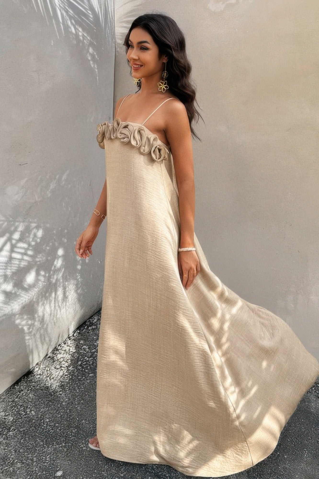Side view of model in flowing sand-toned maxi dress with soft light and shadows in background