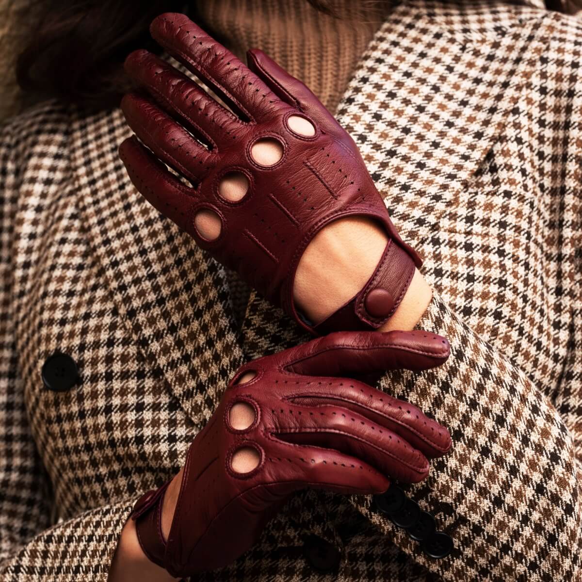 Pair of maroon leather gloves worn by a person in a checkered coat.