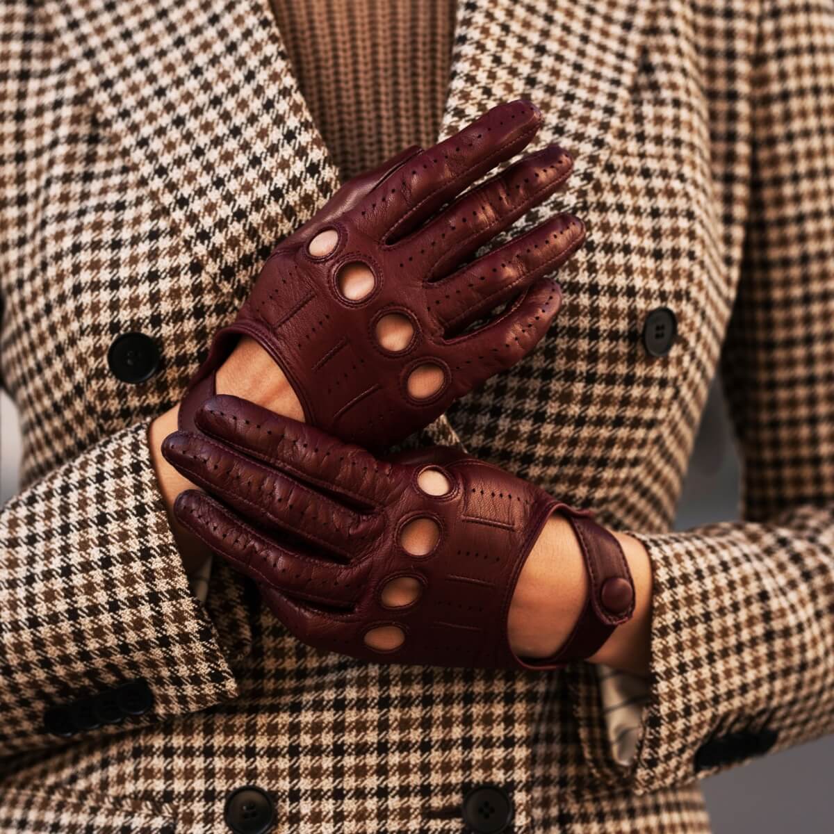 Brown leather gloves with cut-out design worn by a person in a checkered coat.
