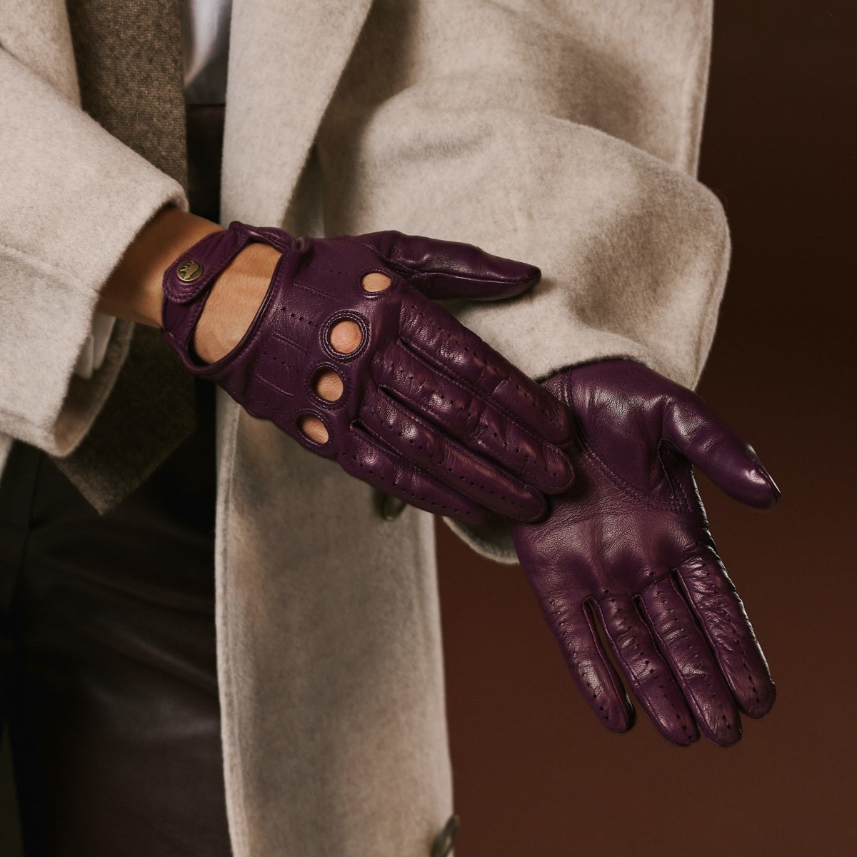 Purple leather gloves worn with a beige coat on a dark background