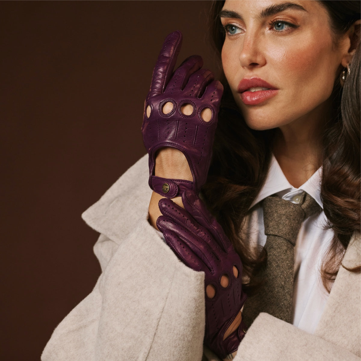 Woman wearing a beige coat and purple leather gloves against a brown background