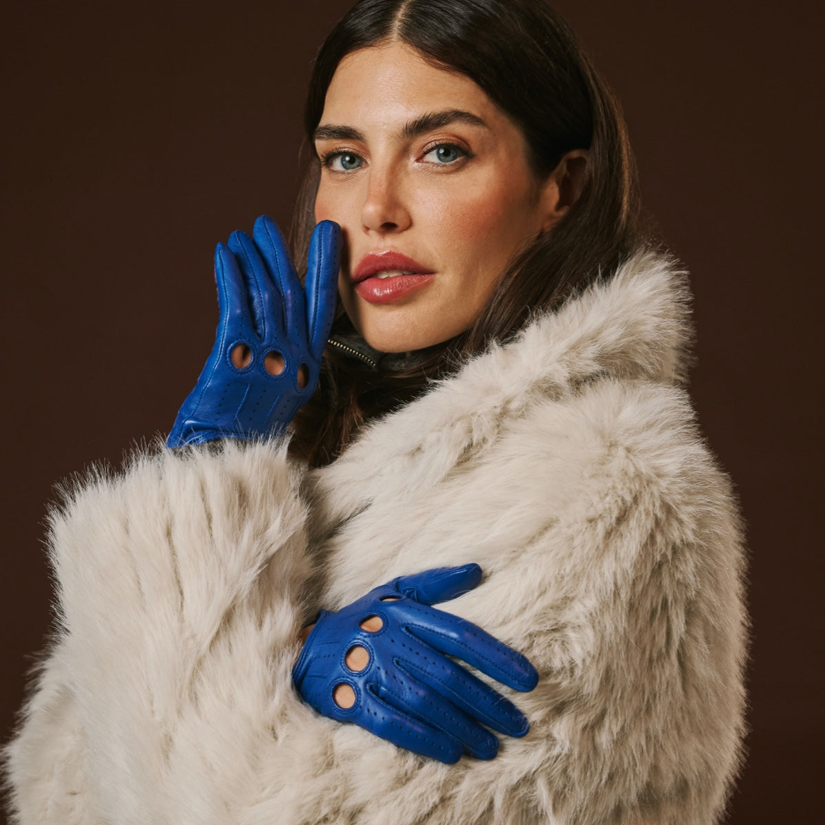 Woman wearing a fur coat and blue leather gloves against a brown background