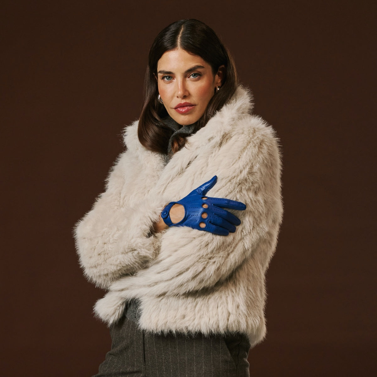 Woman wearing a beige fur coat and blue gloves against a brown background