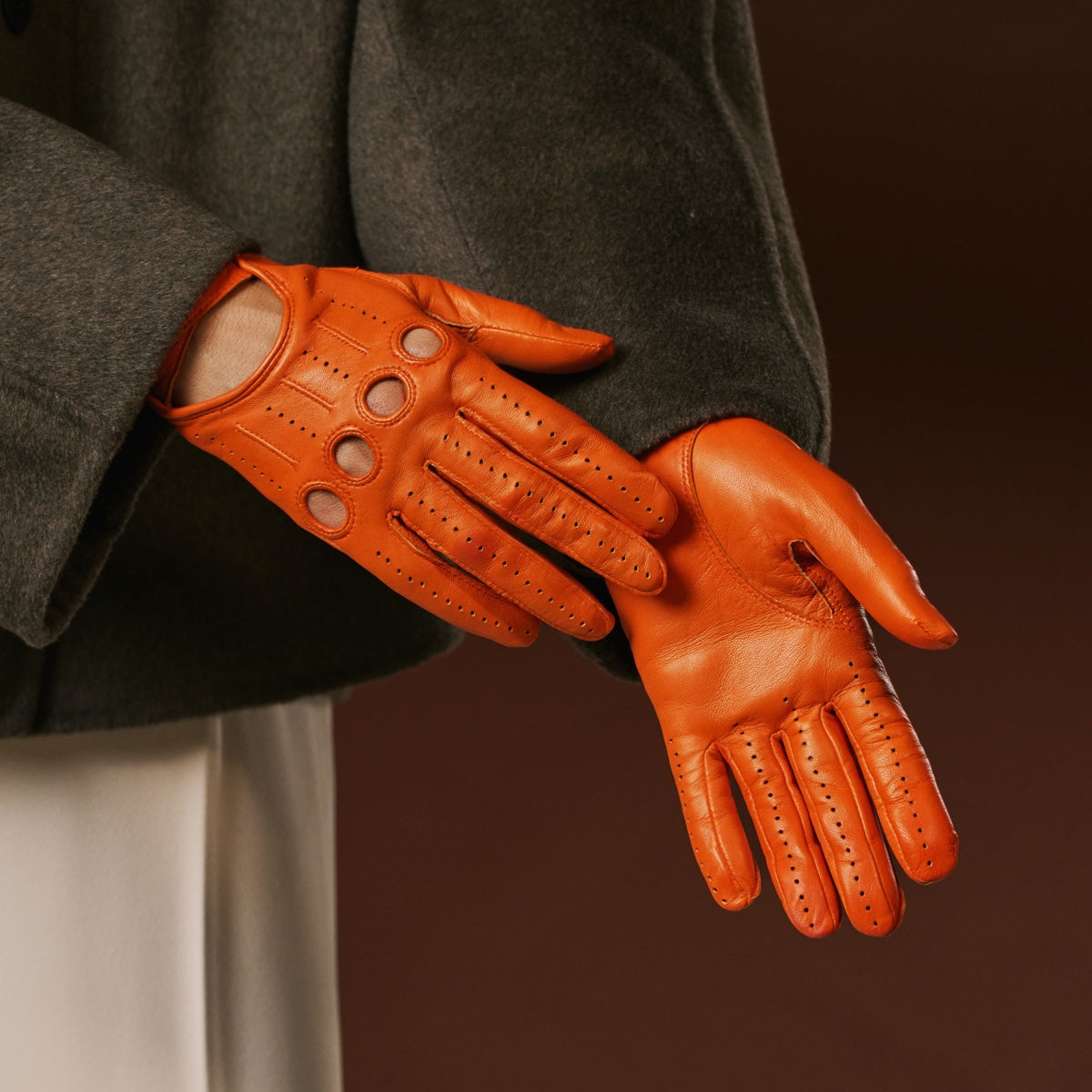 Orange leather gloves worn by a person against a dark background