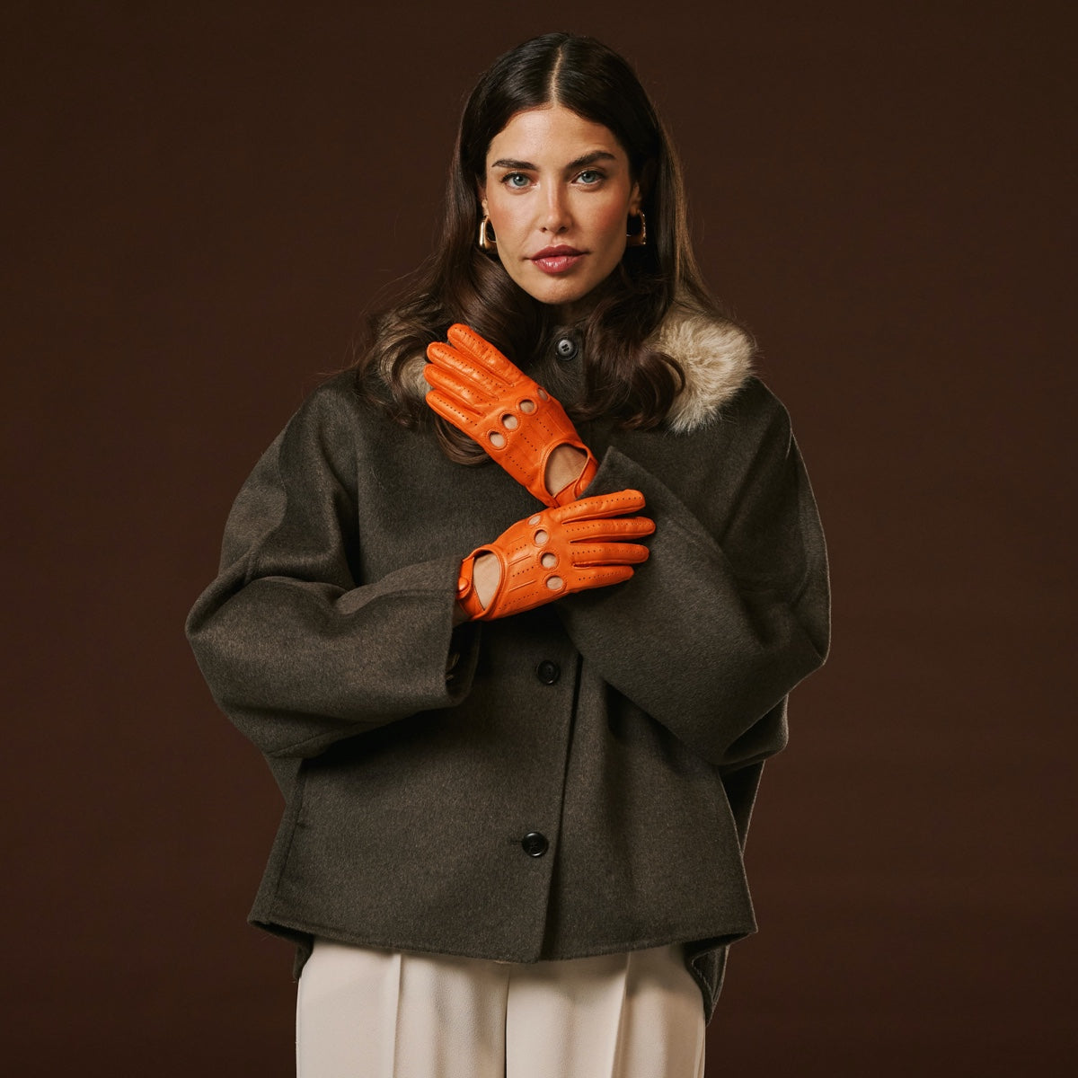Woman wearing a dark coat and orange gloves against a brown background