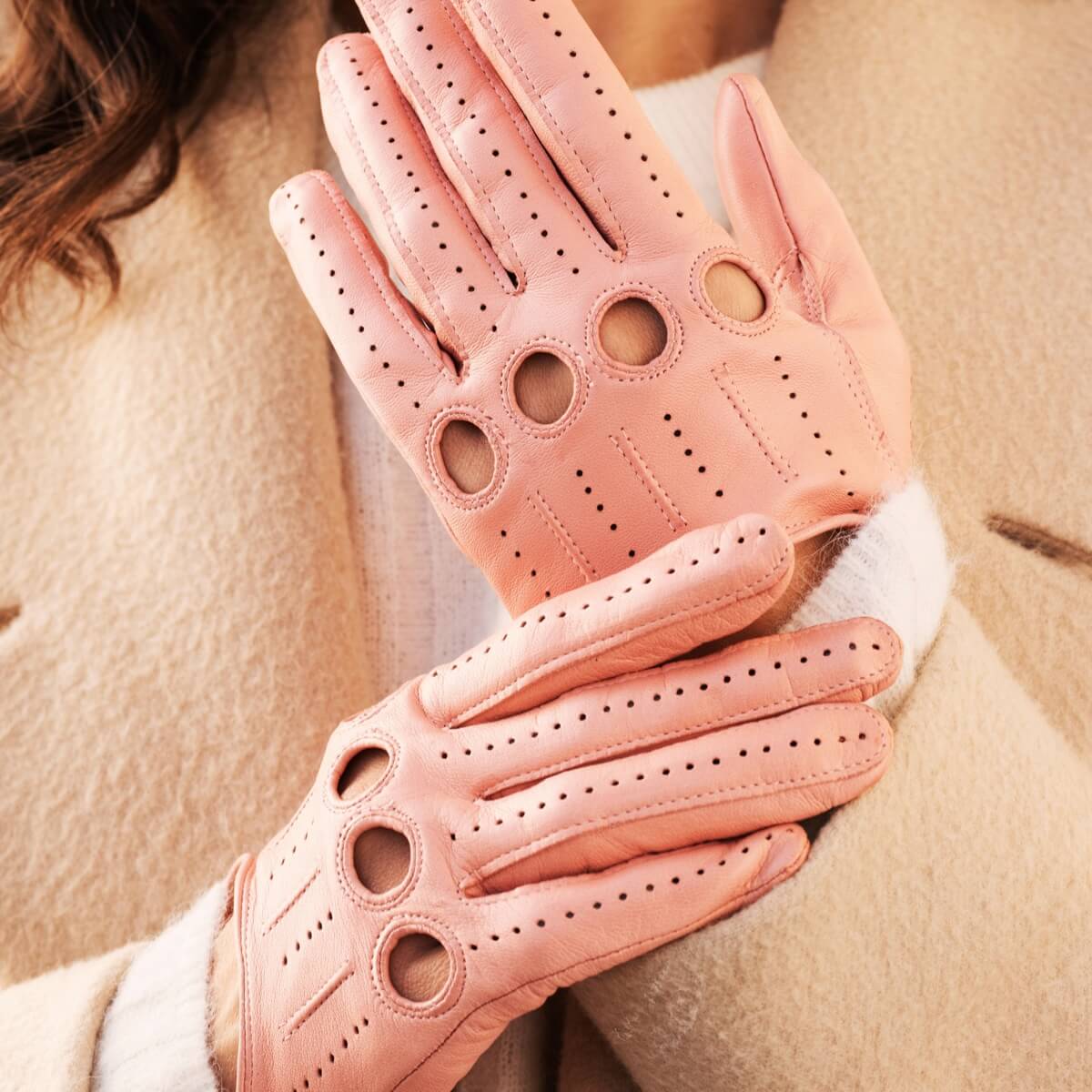 Pink leather gloves with cut-out design worn by a person in a beige coat.