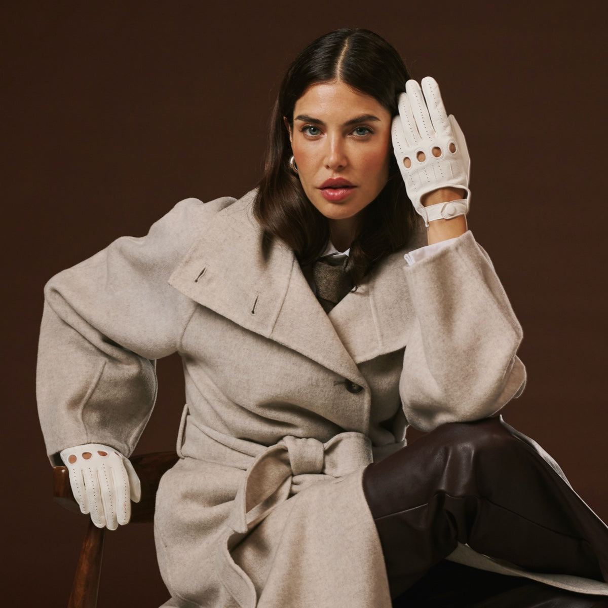Woman wearing a beige coat and white leather gloves against a brown background