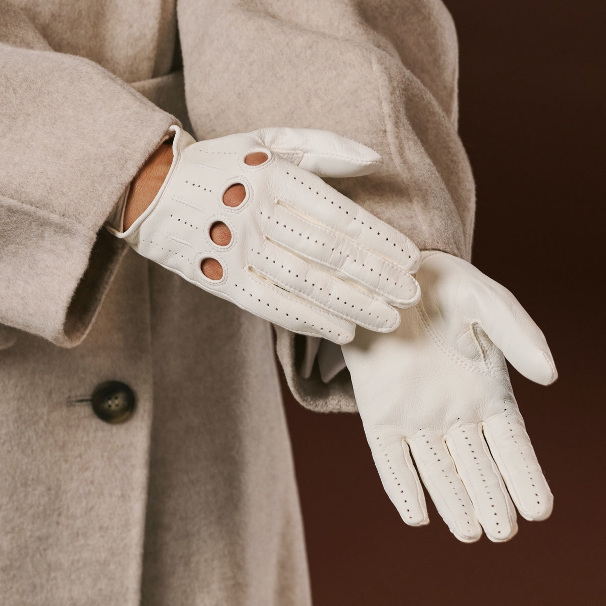White leather gloves worn with a beige coat on a dark background