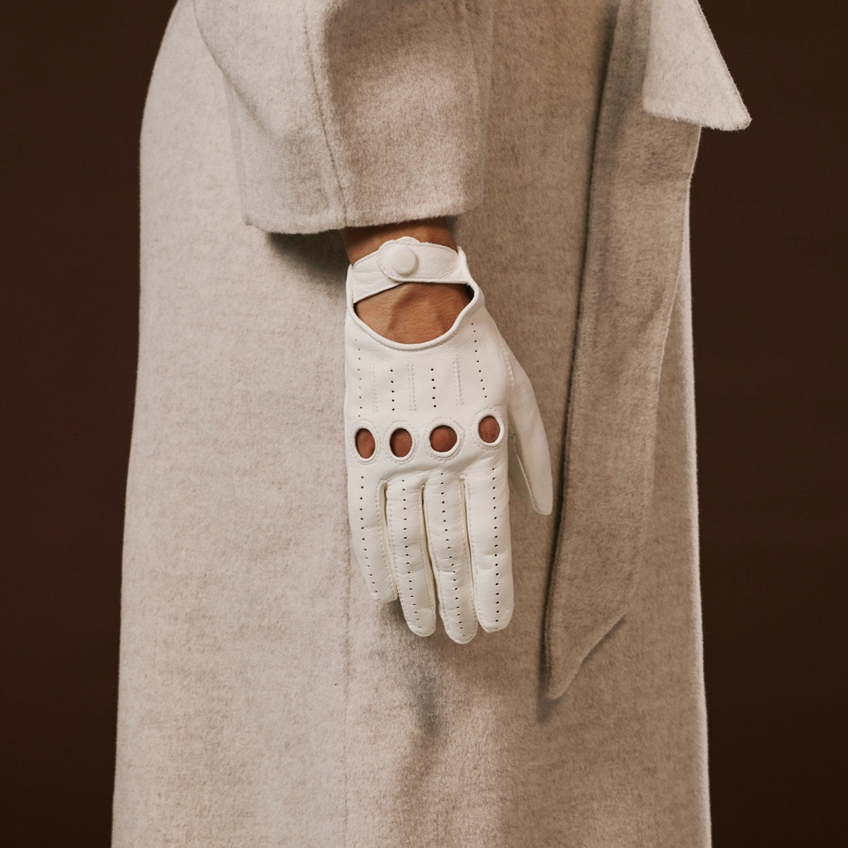 White leather glove with brown buttons on a person wearing a beige coat against a dark background