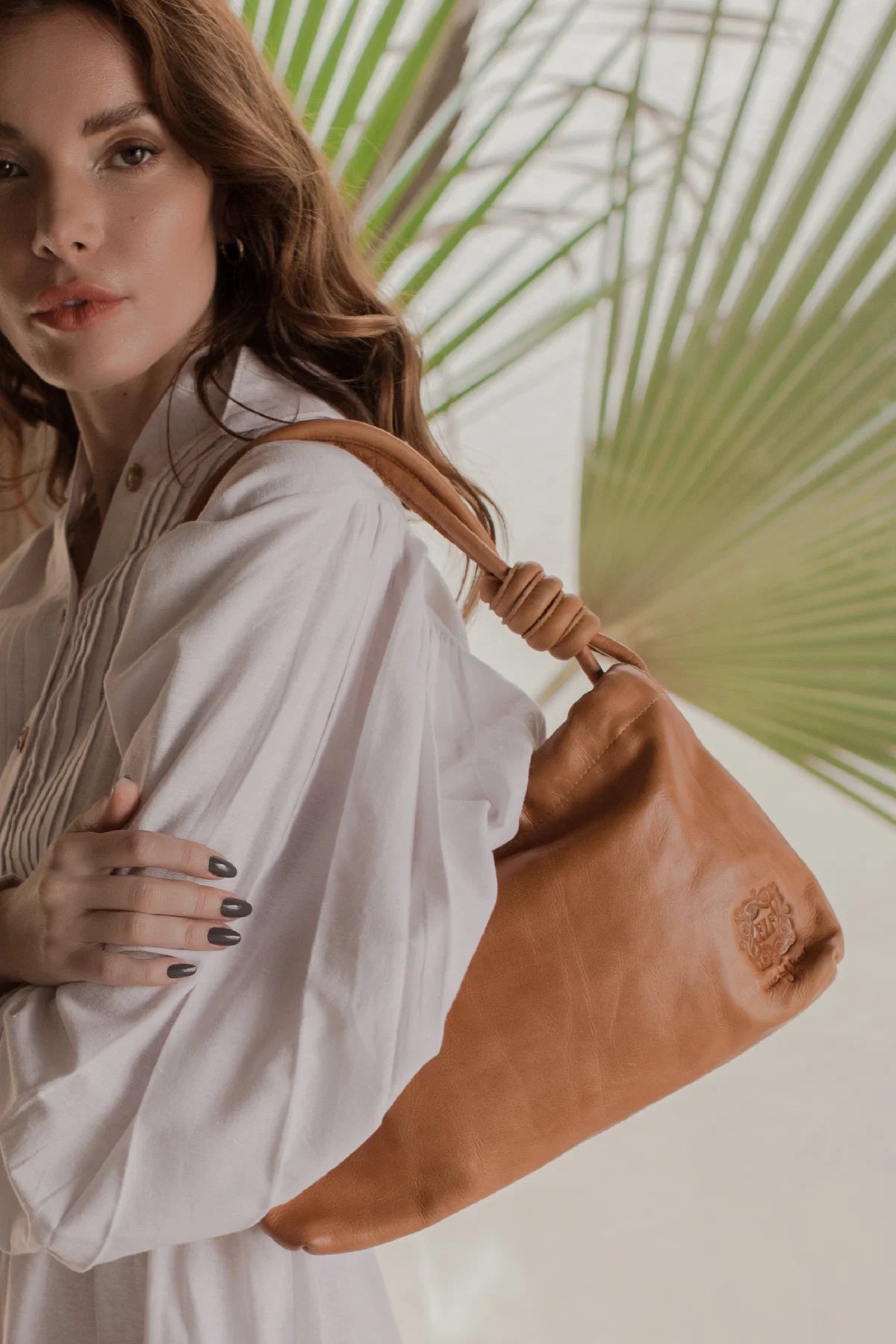 Woman holding a tan leather bag with a palm leaf in the background