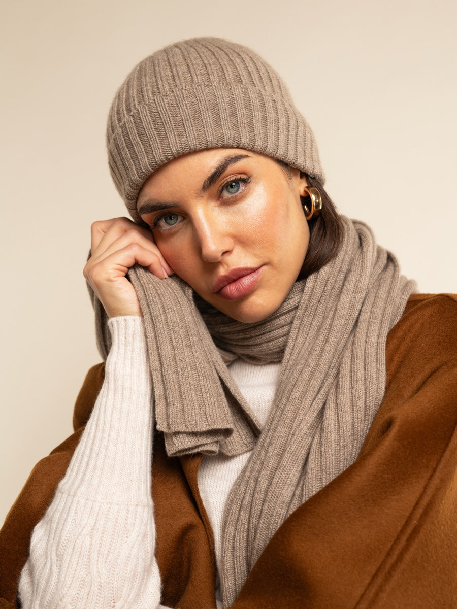 Woman wearing a brown knit beanie and scarf against a beige background