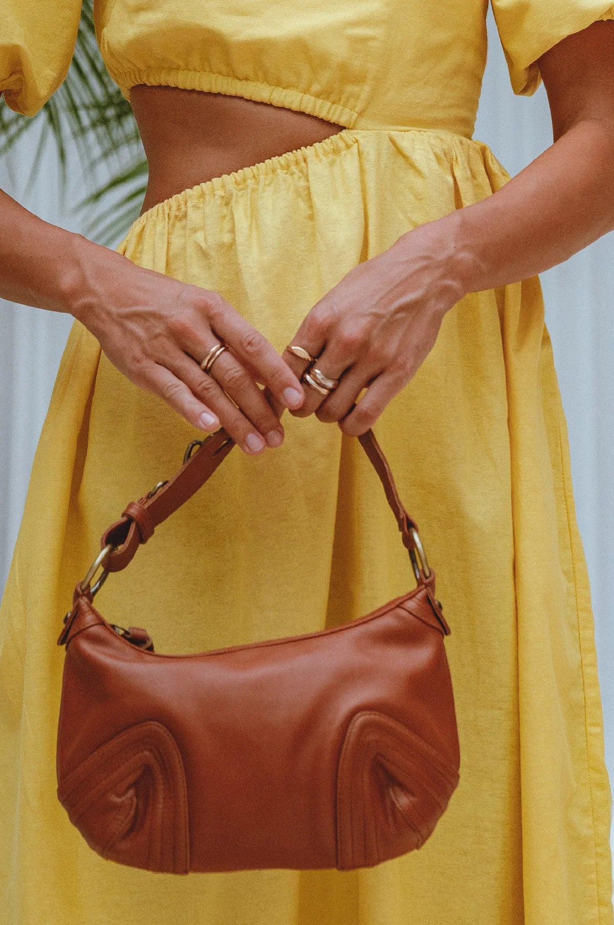 Person wearing a yellow dress holding a camel handbag with a blurred background