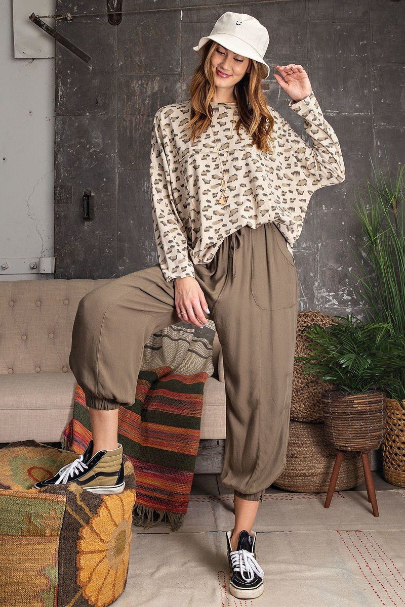 Model in a beige leopard print oversized knit top with dolman sleeves and round neckline, paired with khaki jogger pants and sneakers.