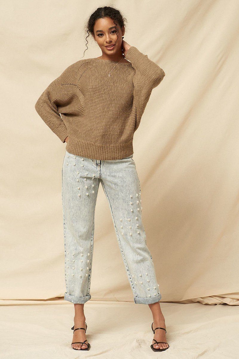 Model in a taupe rib knit boatneck sweater styled with pearl detail light wash jeans and strappy black heels, standing against a neutral backdrop-AVAH