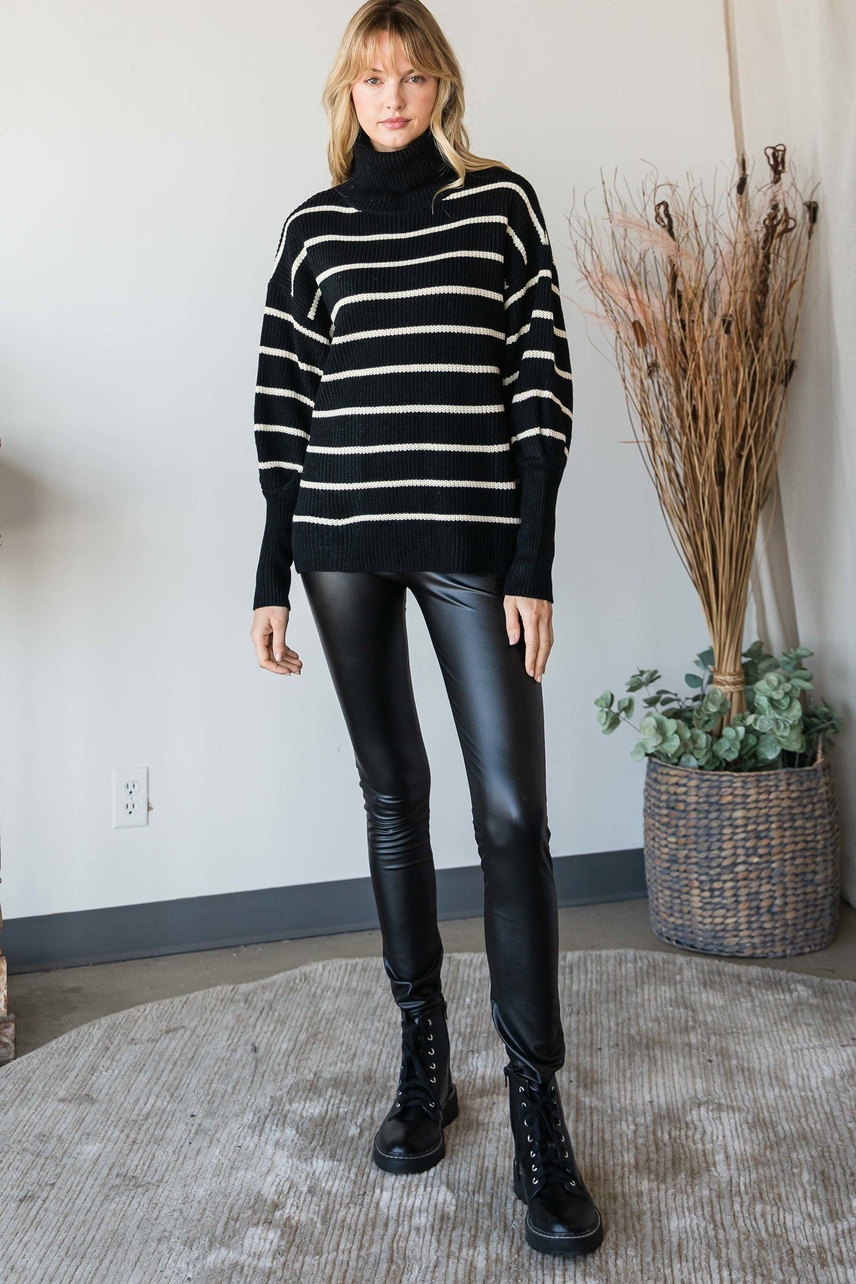 Full-body view of model in a black and ivory striped turtleneck sweater styled with black faux-leather leggings and black combat boots.