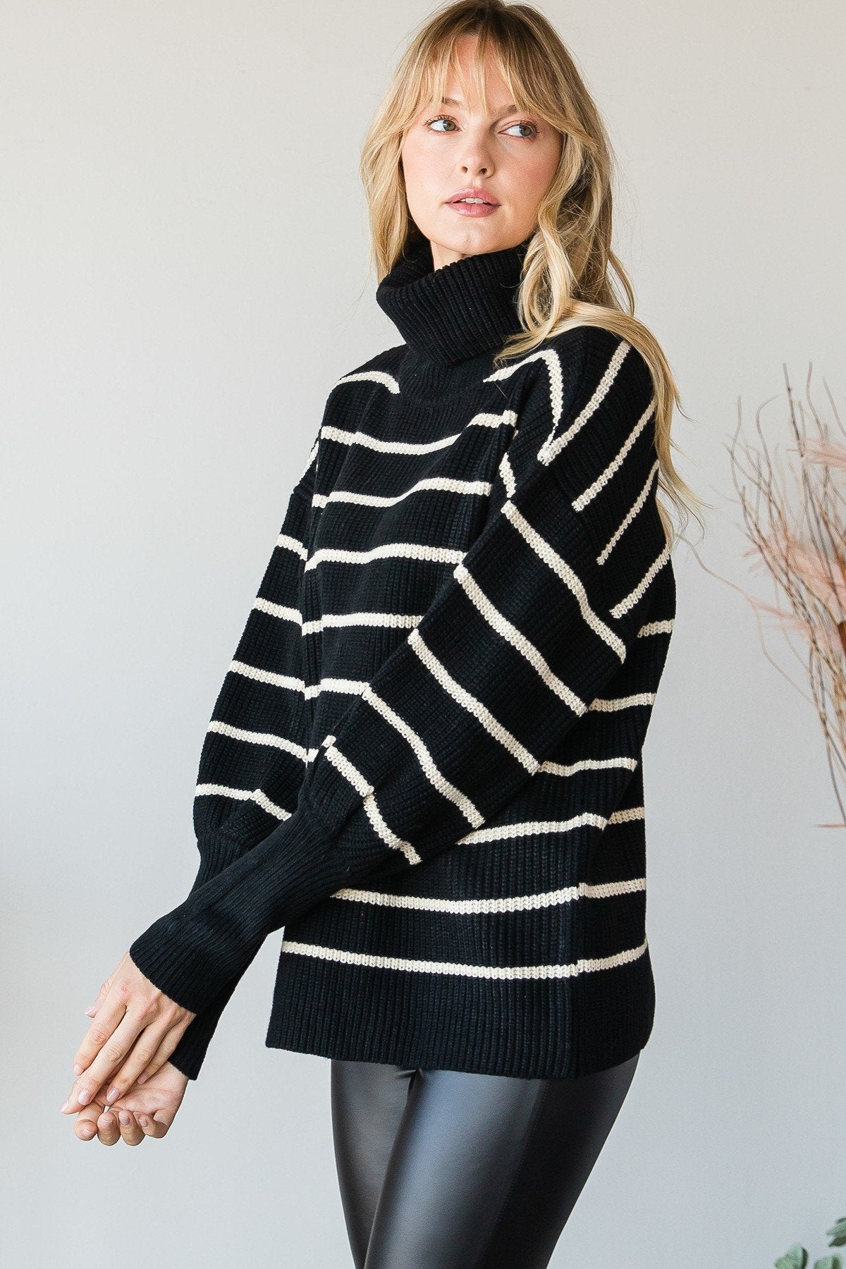 Side angle of model in a black oversized striped turtleneck sweater with relaxed sleeves and ribbed texture.
