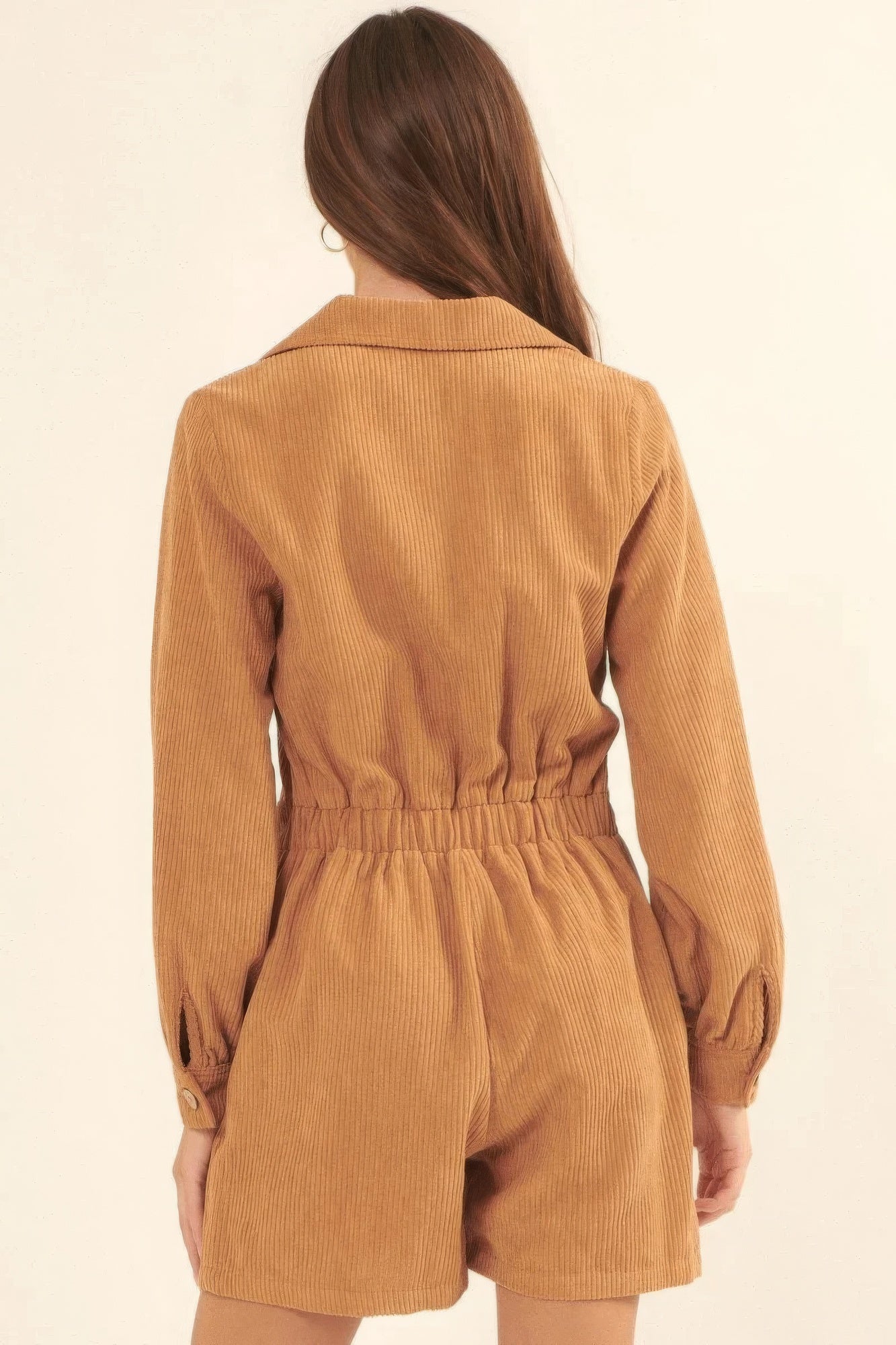 Back of the tan corduroy romper featuring an elastic waistline and long sleeves with button cuffs.