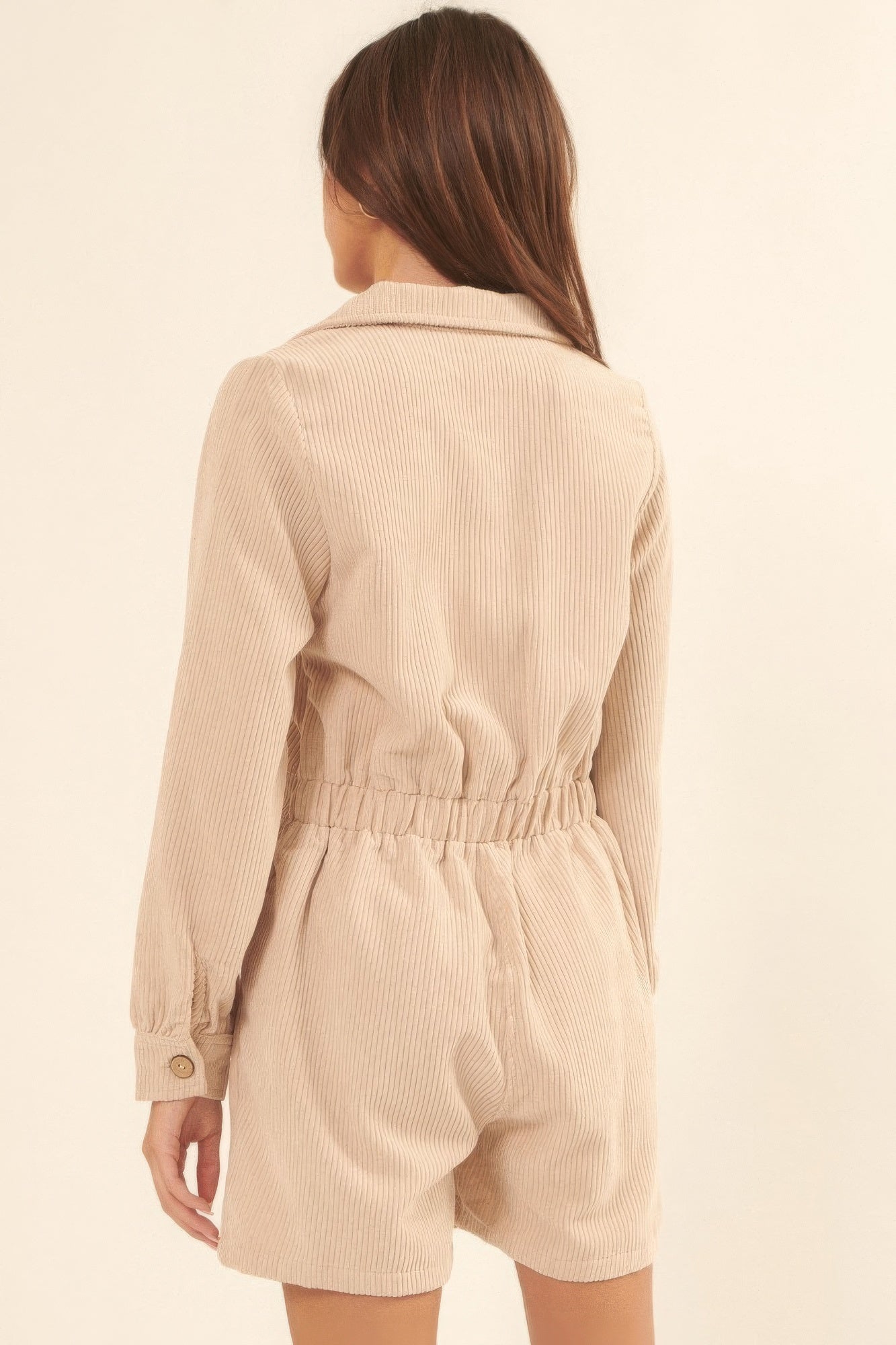 Back view of cream romper with elastic waistband and relaxed long sleeves.