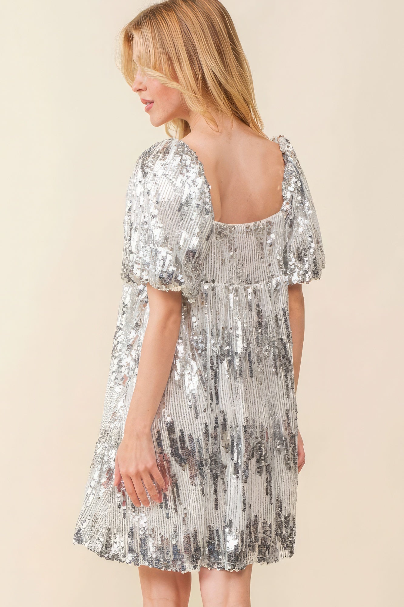 Back view of silver sequin mini dress with square back and puff sleeves.
