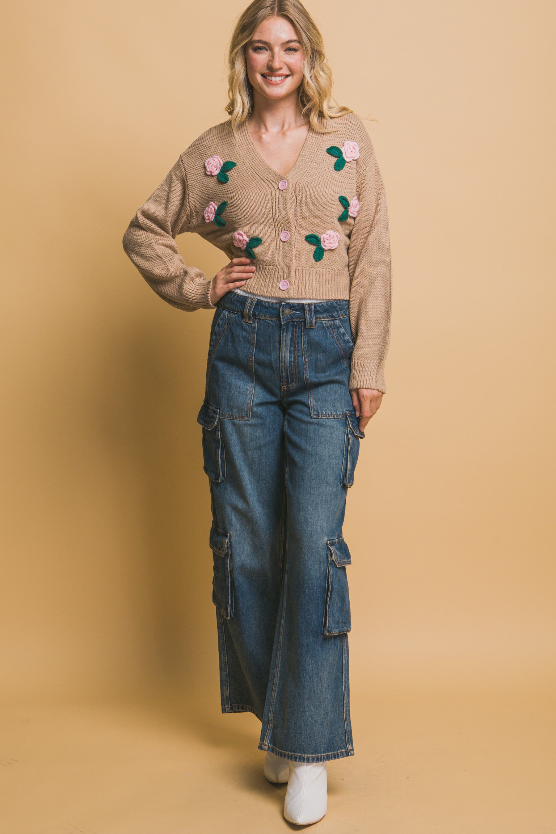 Full front view of a model wearing a khaki cropped cardigan with button-up closure and floral appliqués, paired with wide-leg denim cargo pants.