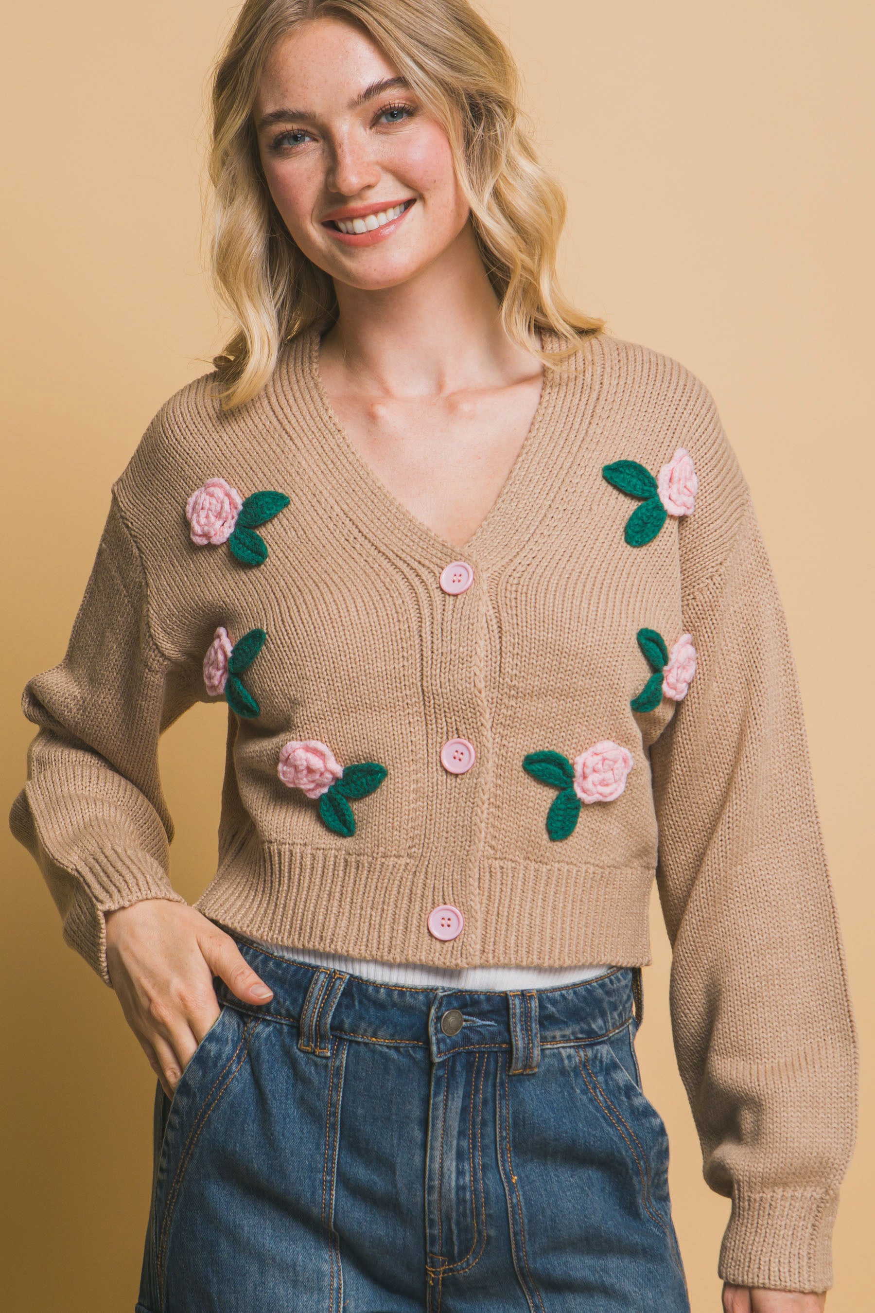 Close-up of open buttoned khaki cropped cardigan with floral appliqués, styled with denim jeans.