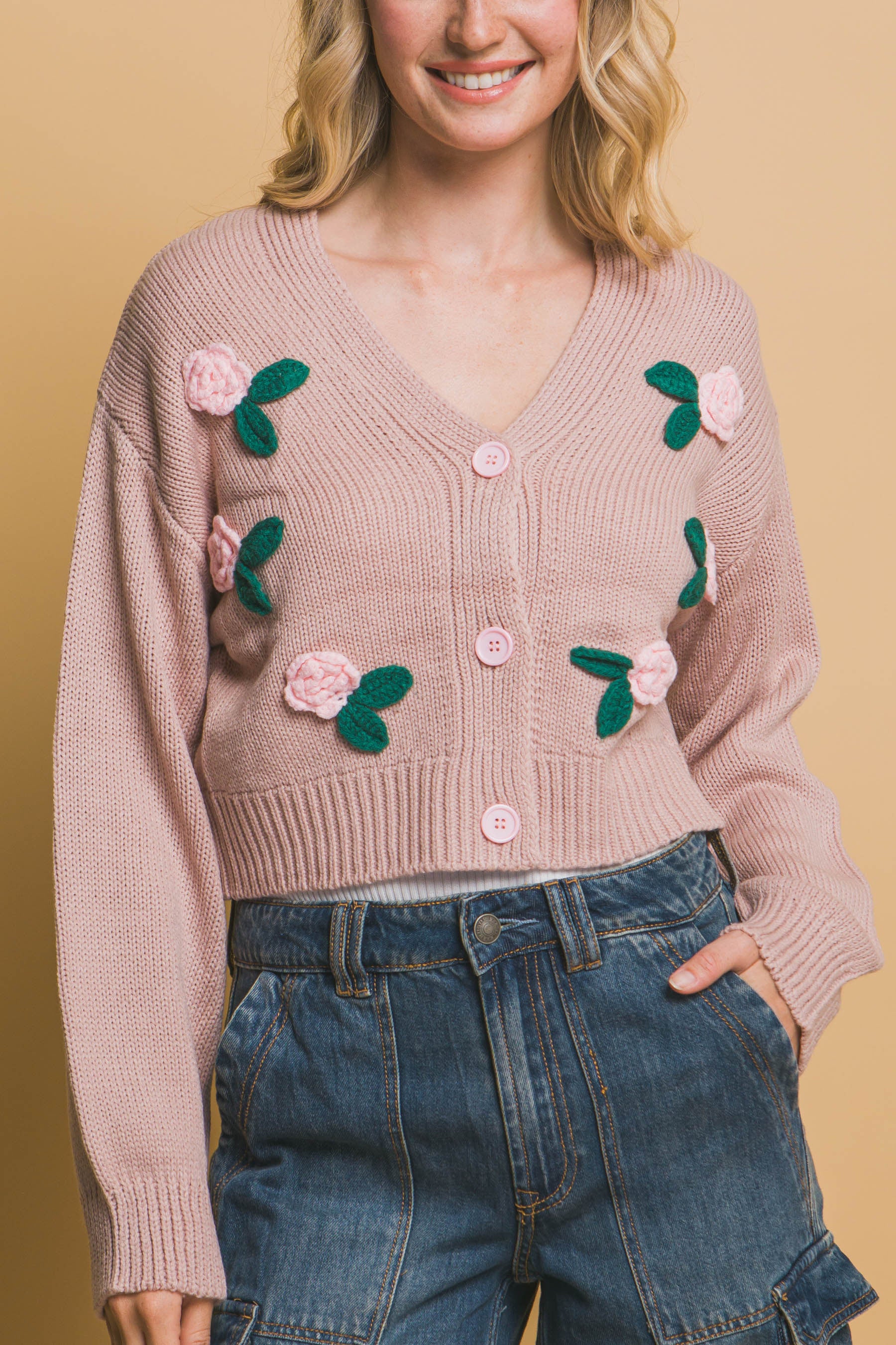 close up of pink sweater with floral and leaf patterns on a beige background