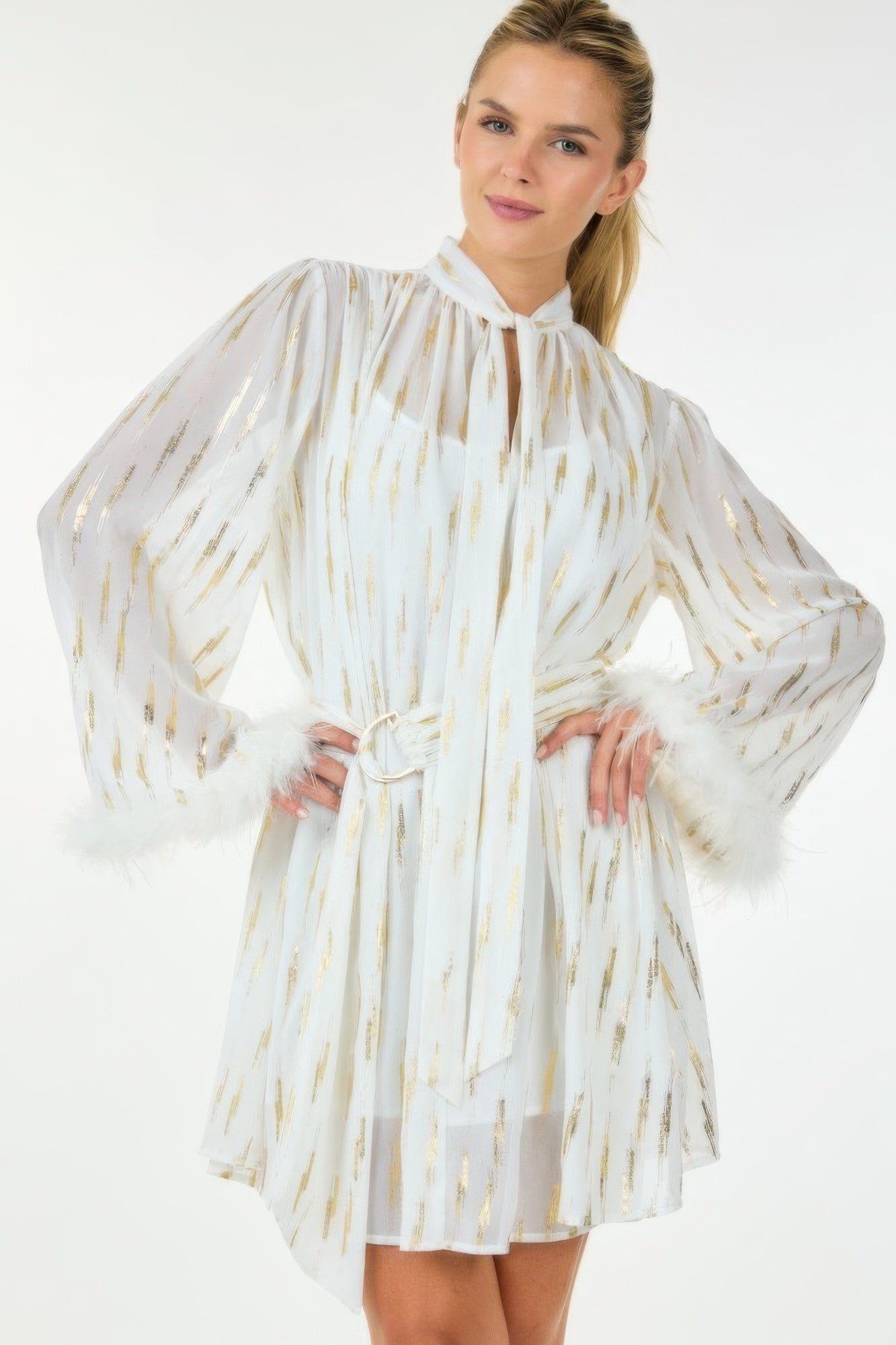 Model wearing white and gold feather-trim mini dress with tie neck and belted waist, front view.