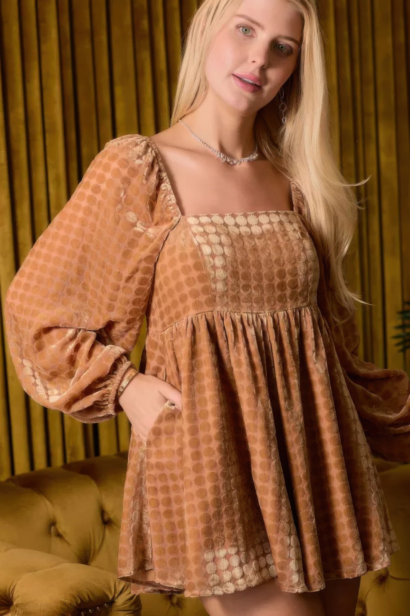 Model wearing a camel patterned romper with long sleeves in a warm-toned room.