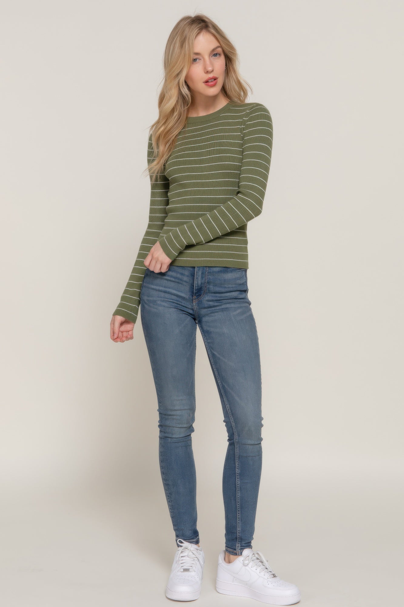 Full-body view of model in an olive striped ribbed top paired with light wash skinny jeans and white sneakers.