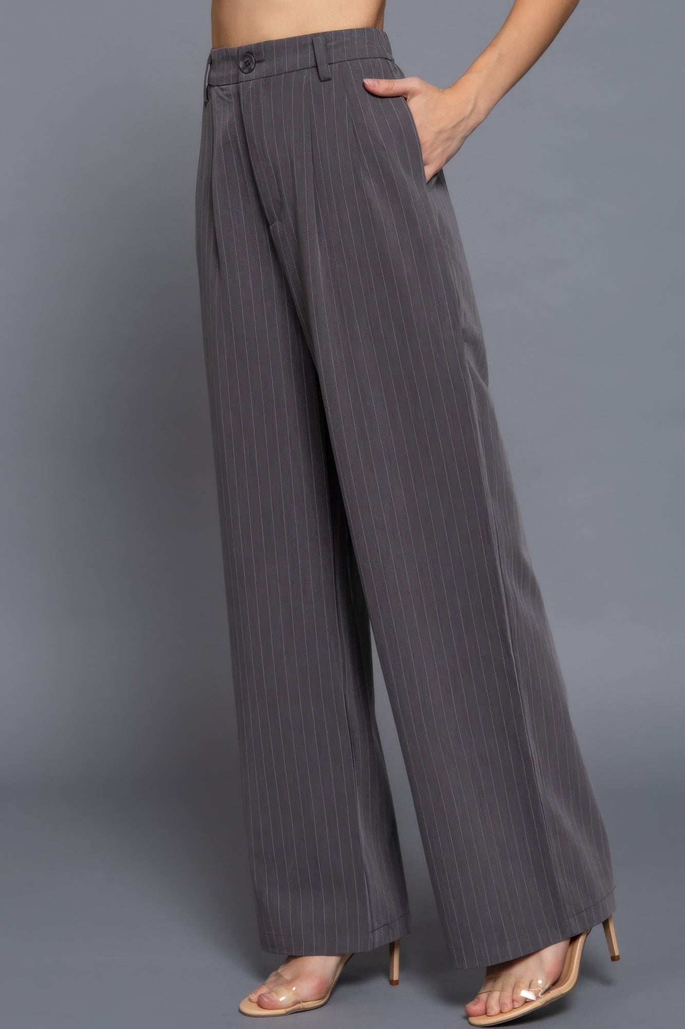 Side view of wide-leg charcoal pinstripe pants highlighting relaxed tailored silhouette and pockets.