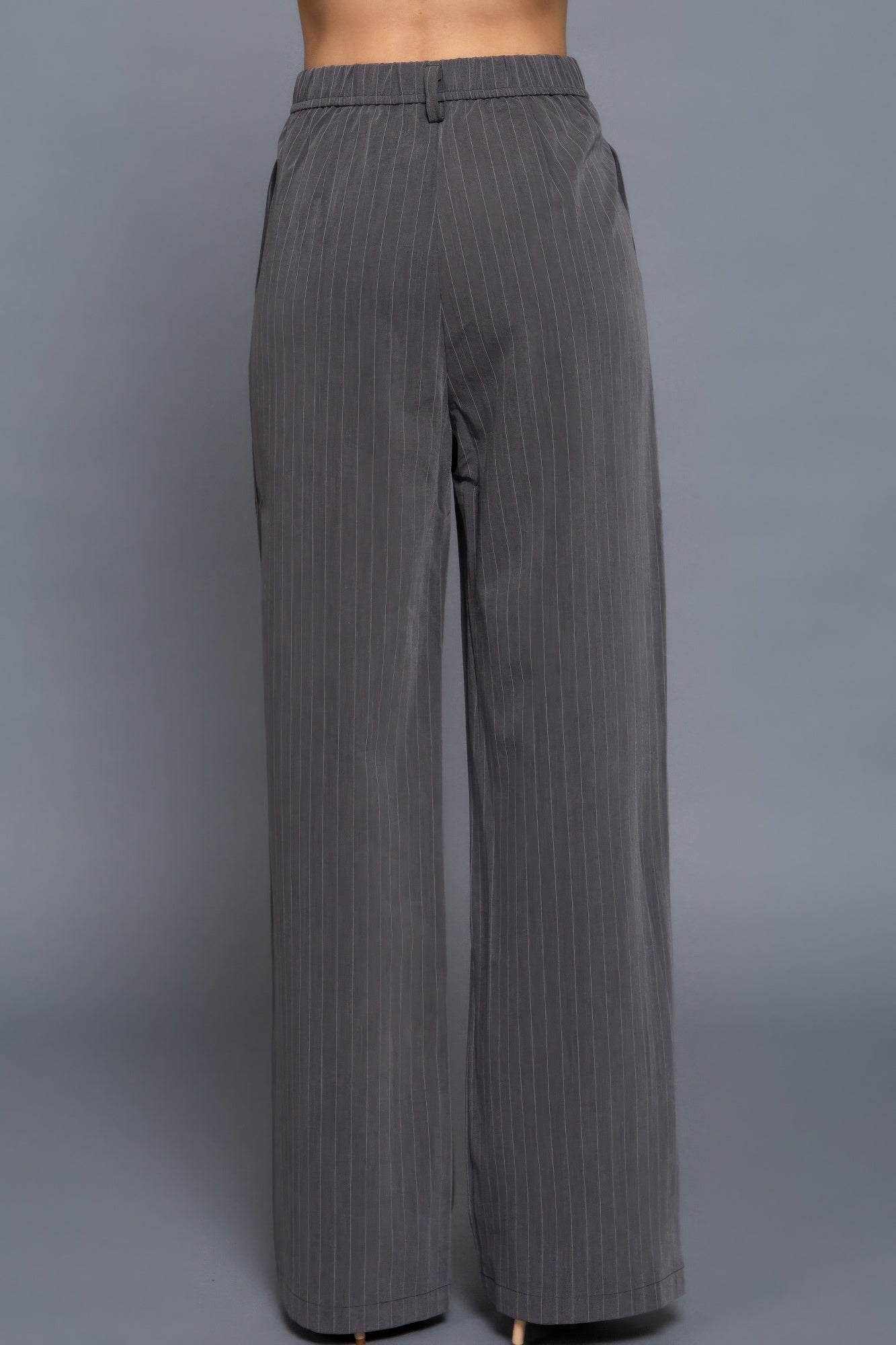 Rear view of charcoal pinstripe trousers with elasticized waistband and straight wide-leg fit.