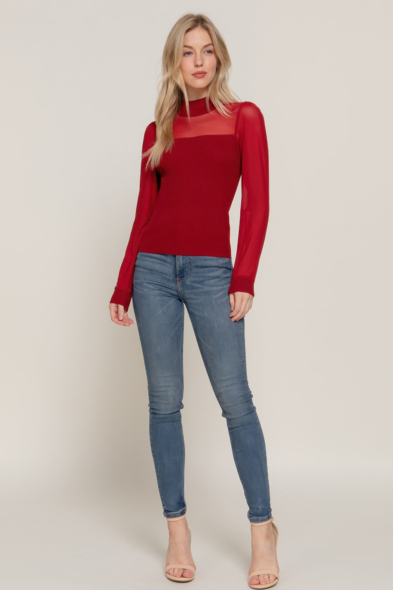 Woman wearing a red long-sleeve top and blue jeans on a plain background