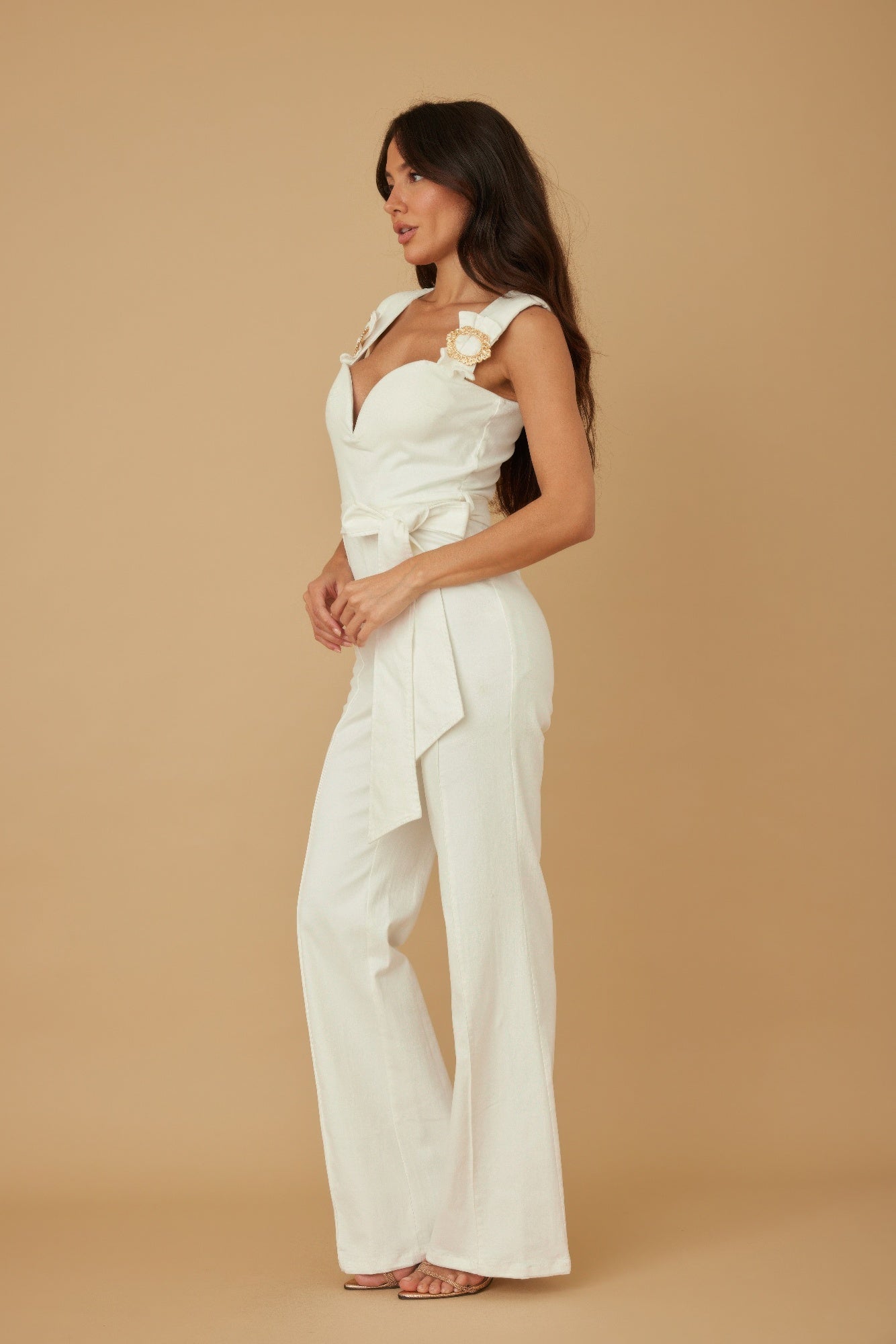 Side view of white bustier wide leg jumpsuit with tie waist and ornate gold buckle straps, AVAH