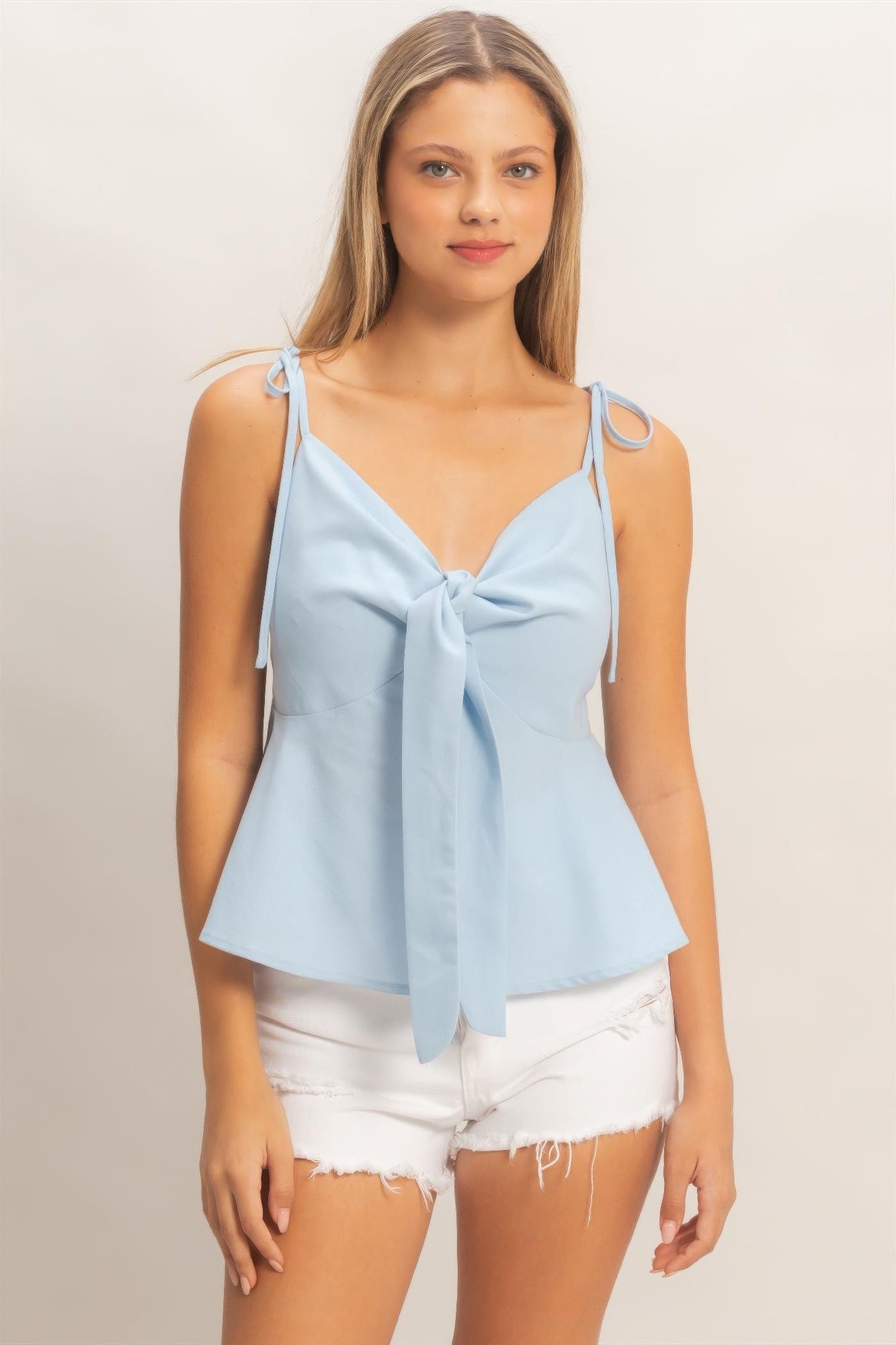 Woman wearing light blue tie front peplum cami top with white distressed shorts